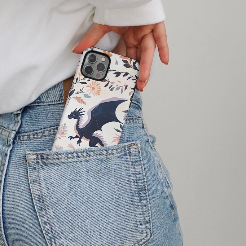 May include: A white phone case with a floral design and a black dragon illustration. The case is in a back pocket of blue jeans.