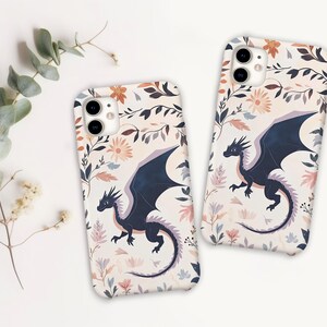 May include: Two phone cases with a floral pattern and a black dragon design. The cases are white with pink, blue, and yellow flowers.