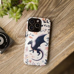 May include: A white phone case with a black dragon and floral pattern. The phone case has a camera lens cutout and a black border.