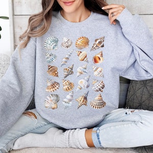 May include: A grey sweatshirt featuring a pattern of assorted seashells in shades of brown, white, and beige.