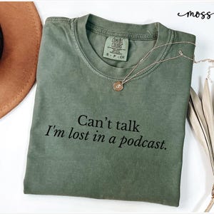May include: A green t-shirt with the text "Can't talk I'm lost in a podcast." printed on it.