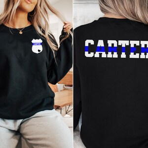 K&ouml;nnte beinhalten: Schwarzer Pullover mit einem blauen Streifen und dem Namen "CARTER" auf der R&uuml;ckseite. Die Vorderseite des Pullovers hat ein wei&szlig;es Abzeichen mit dem Namen "CARTER" und einem blauen Streifen.