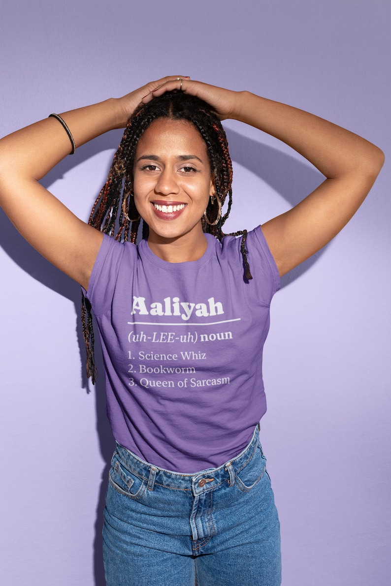Pu&ograve; includere: Una maglietta viola con il nome "Aaliyah" stampato in bianco, insieme a una definizione e tre tratti: Science Whiz, Bookworm e Queen of Sarcasm. La persona indossa jeans blu.