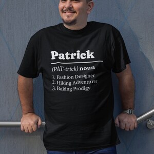 Pu&ograve; includere: T-shirt nera con il nome "Patrick" in bianco, seguito da una definizione. La definizione elenca "Fashion Designer", "Hiking Adventurer" e "Baking Prodigy". La persona indossa jeans blu e un orologio.
