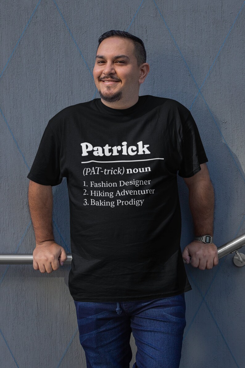 Pu&ograve; includere: T-shirt nera con il nome "Patrick" in bianco, seguito da una definizione. La definizione elenca "Fashion Designer", "Hiking Adventurer" e "Baking Prodigy". La persona indossa jeans blu e un orologio.