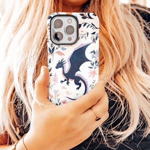 May include: A white phone case with a floral pattern and a black dragon design.