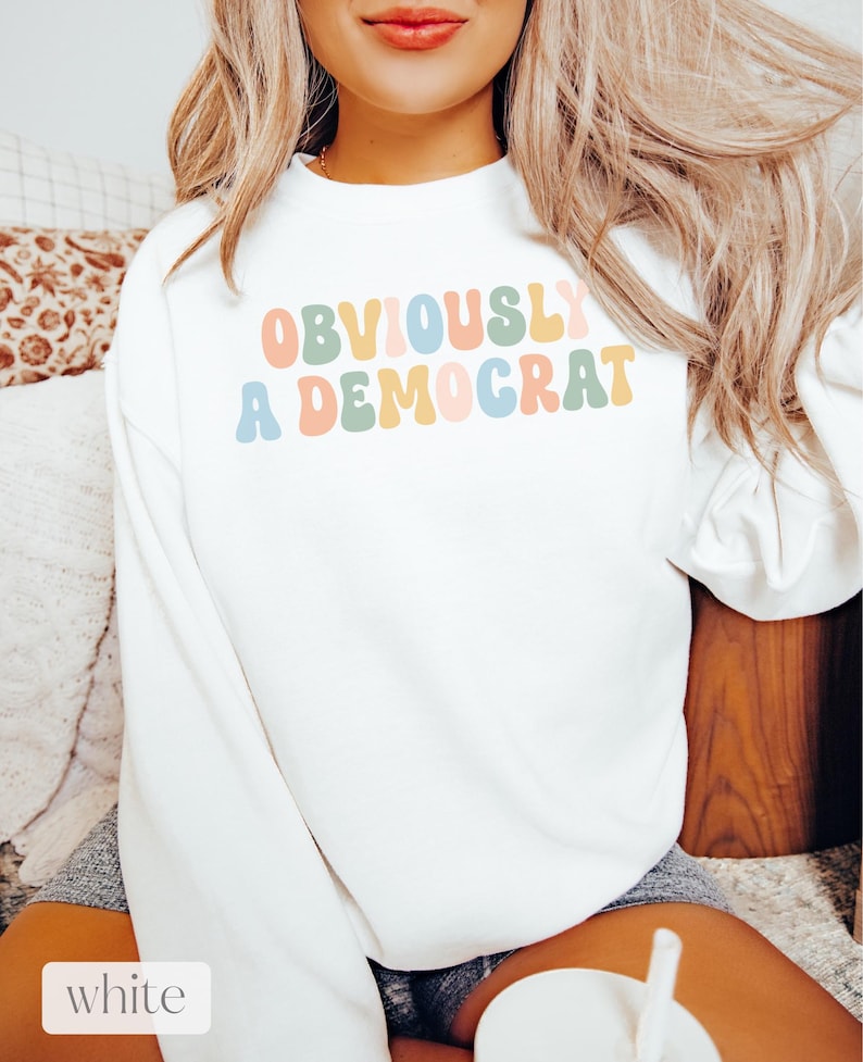 May include: White sweatshirt with the text "OBVIOUSLY A DEMOCRAT" in colorful, retro-style lettering.