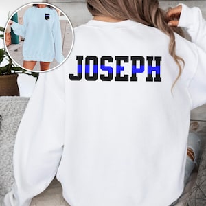 K&ouml;nnte beinhalten: Wei&szlig;er Pullover mit einem blauen Streifen und dem Namen "JOSEPH" auf der R&uuml;ckseite.