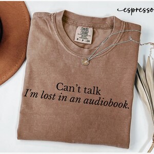 May include: A brown t-shirt with the text "Can't talk I'm lost in an audiobook." printed on it.