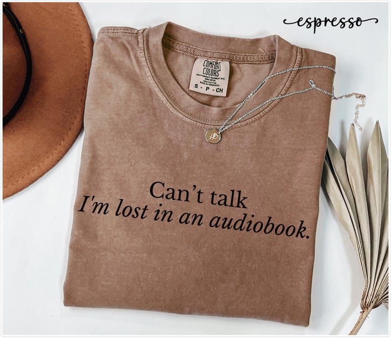 May include: A brown t-shirt with the text "Can't talk I'm lost in an audiobook." printed on it.