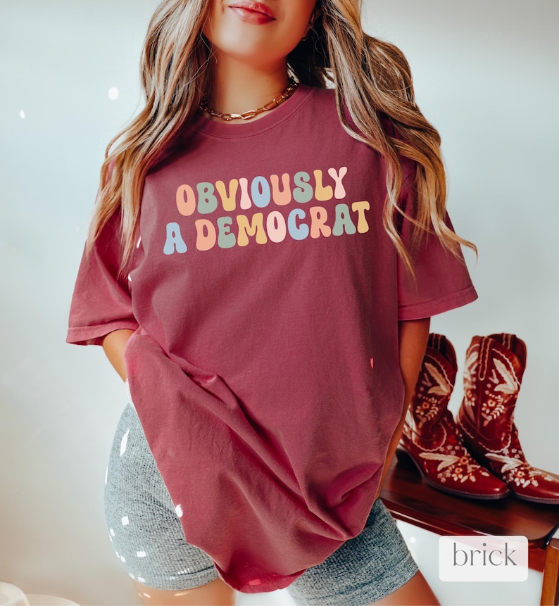 Puede incluir: Una camiseta color granate con el texto "OBVIOUSLY A DEMOCRAT" en letras de colores arco&iacute;ris.