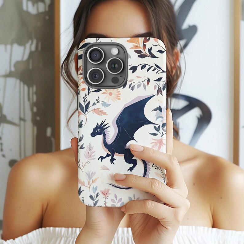 May include: A white phone case with a floral design and a black dragon illustration. The phone case has a camera lens cutout.