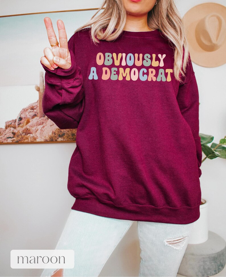 May include: A maroon sweatshirt with the text "OBVIOUSLY A DEMOCRAT" in rainbow-colored letters.