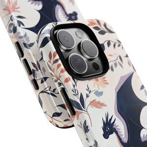 May include: A white phone case with a floral pattern and a black dragon design. The case has a camera lens cutout and a black border.