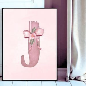 May include: A framed print featuring the letter "J" in a soft pink hue. The letter is adorned with a pink bow and a cluster of flowers and leaves. The background is a lighter shade of pink.