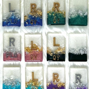 May include: Nine white square tiles with gold and silver glitter embedded in clear resin. Each tile has a letter, 'L' or 'R', and a three-letter code, 'PLO', 'QV', 'QY', 'QW', or 'UZ'.