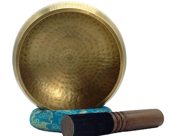 May include: A gold-colored singing bowl with a hammered texture, resting on a blue and gold patterned cushion. A wooden mallet with a black padded head is included.