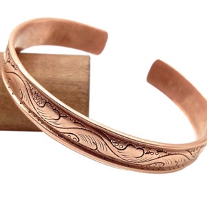 May include: A copper bracelet with a decorative wave pattern engraved around the band.