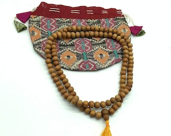 May include: A brown wooden mala bead necklace with a yellow tassel. The necklace is in a colorful patterned pouch.