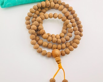 May include: A brown wooden mala bead necklace with a tassel made of orange string. The necklace is made of 108 beads and has a wooden bead at the end of the tassel.