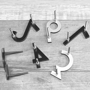 Pu&ograve; includere: Un set di sei numeri civici in metallo, tra cui i numeri 1, 2, 3, 4, 5 e 7. I numeri sono neri e argentati e hanno un design moderno e minimalista.