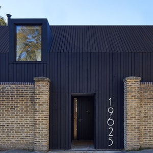 May include: A black modern house with a black door and a window. The house has a brick wall and the number 19025 is displayed on the wall.