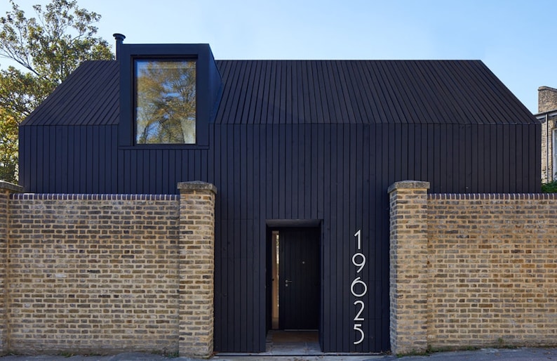 May include: A black modern house with a black door and a window. The house has a brick wall and the number 19025 is displayed on the wall.