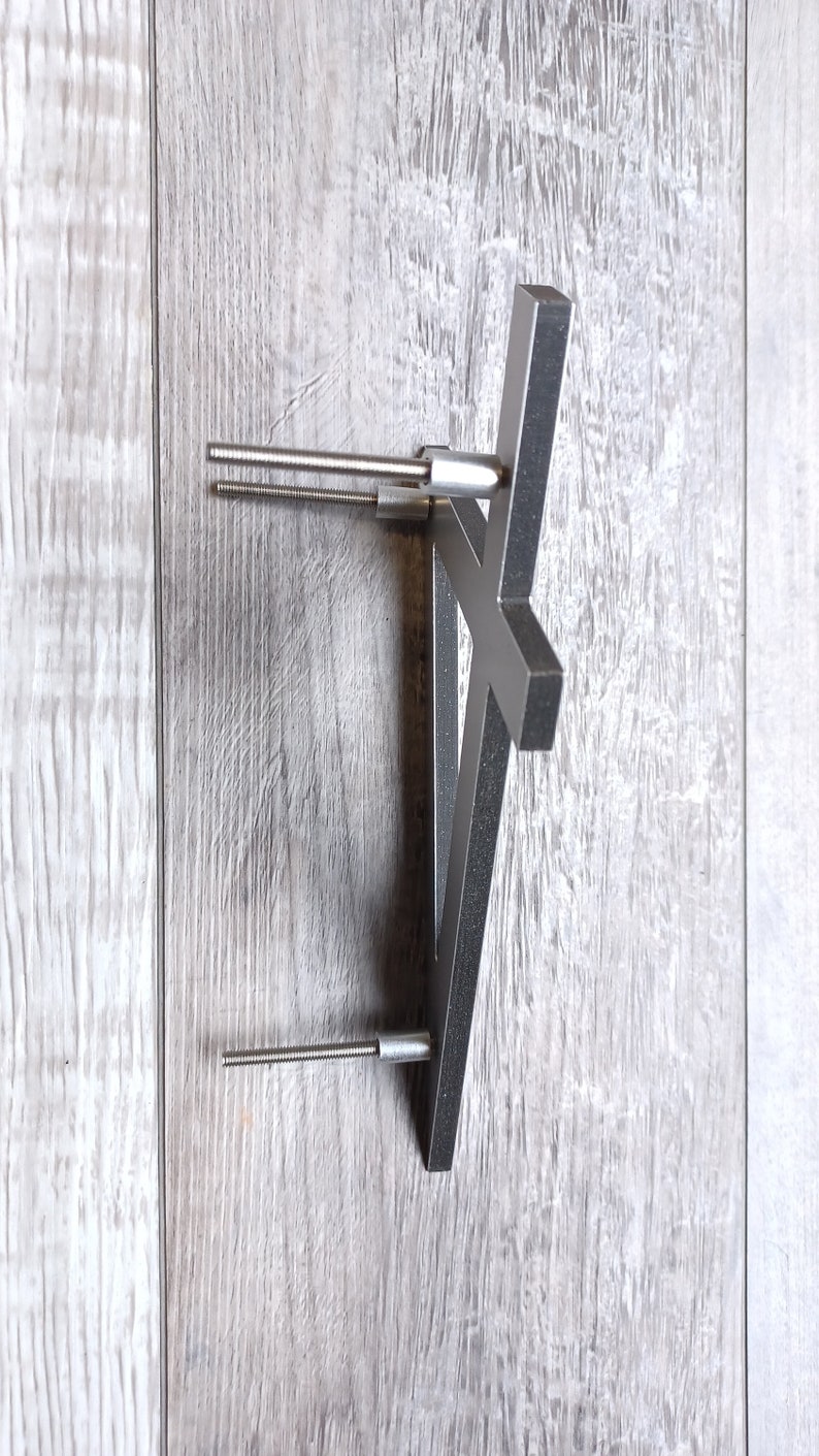 May include: A silver metal shelf bracket with two screws attached to a light gray wood surface.