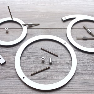 May include: Three white metal circles with holes and small metal rods, some of which are attached to the circles. The circles are arranged in a triangular pattern on a wood surface.