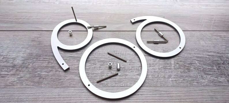 May include: Three white metal circles with holes and small metal rods, some of which are attached to the circles. The circles are arranged in a triangular pattern on a wood surface.