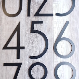 May include: Black metal house numbers 0 through 9. The numbers are modern and minimalist in style.