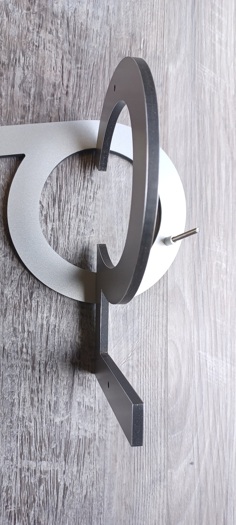 May include: A silver metal house number with a black metal bracket. The number is a "C" and is attached to the bracket with a screw.