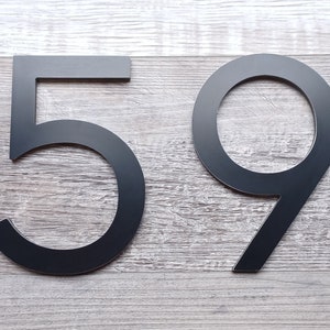 May include: Black metal house numbers 59 on a woodgrain background.