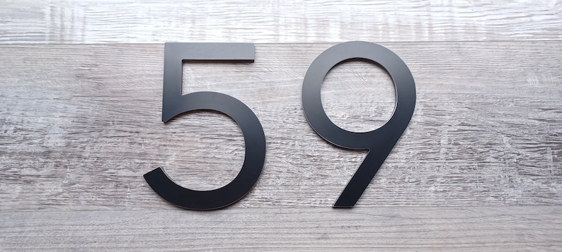 May include: Black metal house numbers 59 on a woodgrain background.