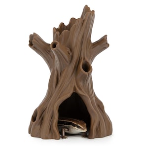 Può includere: Un rifugio per rettili a forma di tronco d'albero marrone con più aperture. Il rifugio ha una base scavata dove è visibile una lucertola. Il tronco d'albero ha una superficie strutturata ed è progettato per imitare l'aspetto del legno naturale.