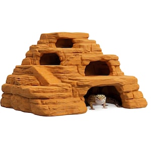May include: A layered, tan-colored reptile habitat resembling a rock formation. The structure has multiple openings and a ramp. A leopard gecko is visible inside the cave-like opening, with its head and front legs showing.