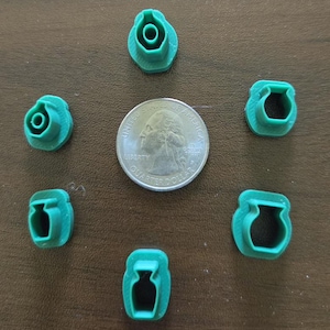May include: Six small green plastic vase-shaped cookie cutters arranged in a circle around a United States quarter dollar coin. Each cutter features a distinct silhouette of a vase, providing a scale reference for their compact size.