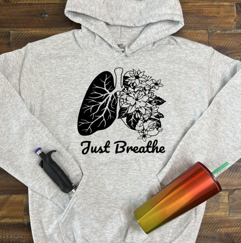 May include: A gray hoodie with a black and white graphic of a lung with flowers growing out of it. The text "Just Breathe" is printed below the graphic.