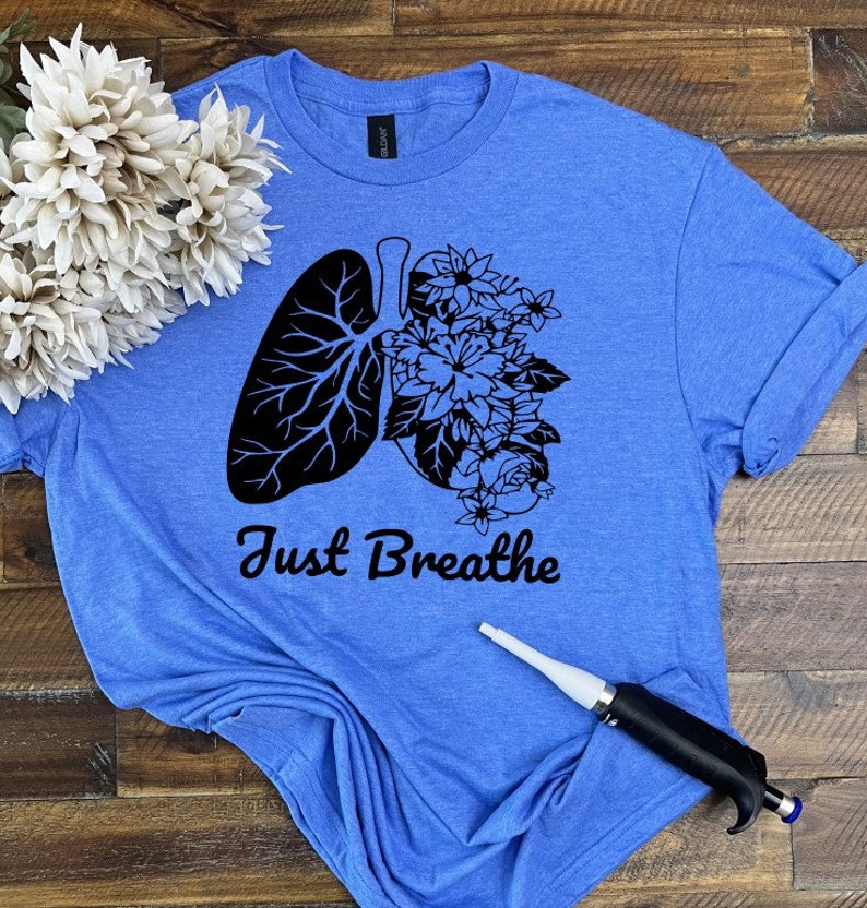 May include: A blue t-shirt with a black graphic of a lung with flowers growing out of it. The text "Just Breathe" is printed below the graphic.