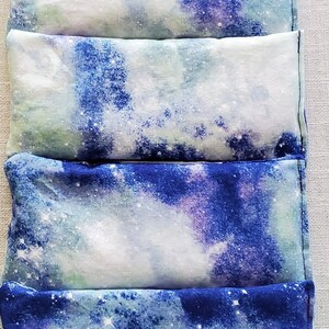 May include: Four blue and white galaxy print eye pillows stacked on top of each other. The pillows are made of soft fabric and have a subtle sheen.