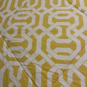 May include: Yellow and white geometric pattern on a quilted fabric. The design features interlocking shapes and lines, creating a repeating pattern. The fabric is a light yellow color with white accents, and the quilting adds texture.