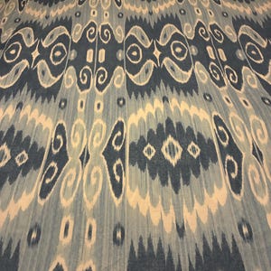 May include: A textile blanket featuring a repeating ikat pattern in shades of dark blue, light blue, and white. The design consists of symmetrical, elongated diamond shapes and swirling motifs arranged in vertical columns across the fabric surface.