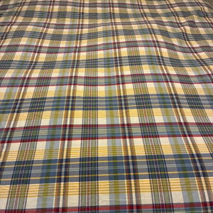 May include: A bedspread with a plaid pattern in shades of blue, yellow, red, and white. The fabric has a soft, slightly wrinkled appearance. The bedspread is spread over a bed with white pillows.