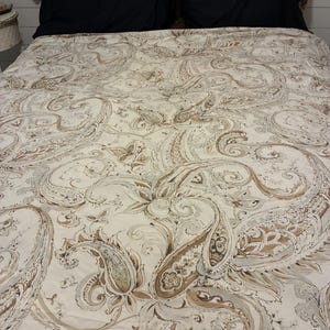 May include: A bedding set featuring a cream-colored duvet cover with a large-scale brown and tan paisley pattern. The bed includes two solid black rectangular pillows positioned in front of two additional pillows with a brown leopard print.