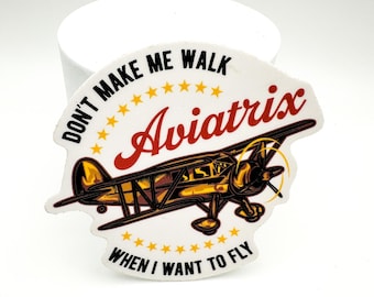 May include: A white sticker with a vintage airplane illustration. The sticker features the text "DON'T MAKE ME WALK WHEN I WANT TO FLY" and the name "Aviatrix" in a stylized font. The airplane is detailed in brown and gold.