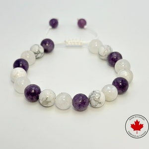 Peut inclure: Un bracelet en perles blanches et violettes avec une fermeture en cordon blanc. Le bracelet est fait de perles rondes et présente un motif marbré blanc et gris.
