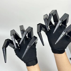 May include: A pair of black gloves with articulated claws. The claws are made of black plastic and are designed to look like a spider's legs.