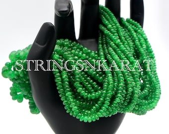 Peut inclure: Un brin de perles de pierres précieuses vertes, probablement de la péridot, présenté sur un support noir en forme de main. Les perles sont petites et rondes, et le brin est long et plein. Le texte "STRINGSNKARAT" est visible sur le support.