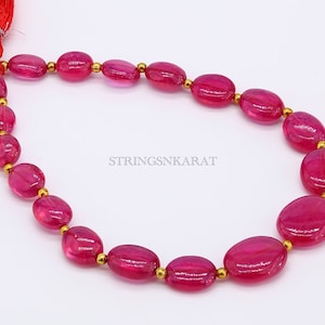May include: A strand of pink oval-shaped gemstone beads with gold spacers. The beads are strung on a cord with a tassel at one end. The text "STRINGSNKARAT" is visible in the image.