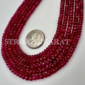 May include: A strand of deep red ruby beads, approximately 4mm in diameter, with a faceted finish. The beads are strung on a clear thread and are displayed next to a US quarter for size reference.